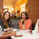 Four women having a friendly branding strategy meeting at a cozy café with notebooks and coffee.