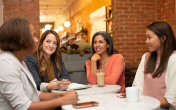 Four women having a friendly branding strategy meeting at a cozy café with notebooks and coffee.