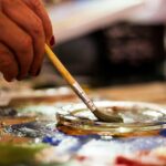 Close-up of a hand dipping a paintbrush into water on a colorful artist palette
