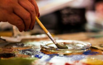 Close-up of a hand dipping a paintbrush into water on a colorful artist palette