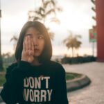Woman wearing a “Don’t Worry” sweatshirt covering one eye outdoors at sunset