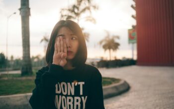 Woman wearing a “Don’t Worry” sweatshirt covering one eye outdoors at sunset