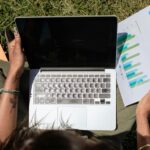 Person working on a laptop outdoors while reviewing sales charts, symbolizing practical and impactful sustainable business practices in 2025.