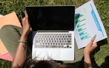Person working on a laptop outdoors while reviewing sales charts, symbolizing practical and impactful sustainable business practices in 2025.