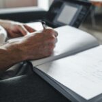 Person writing brand experience strategy notes in a notebook with a laptop nearby, symbolizing creative planning and intentional design.