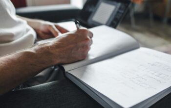 Person writing brand experience strategy notes in a notebook with a laptop nearby, symbolizing creative planning and intentional design.