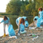 Volunteers collecting litter along a lakeside as part of a social responsibility initiative.
